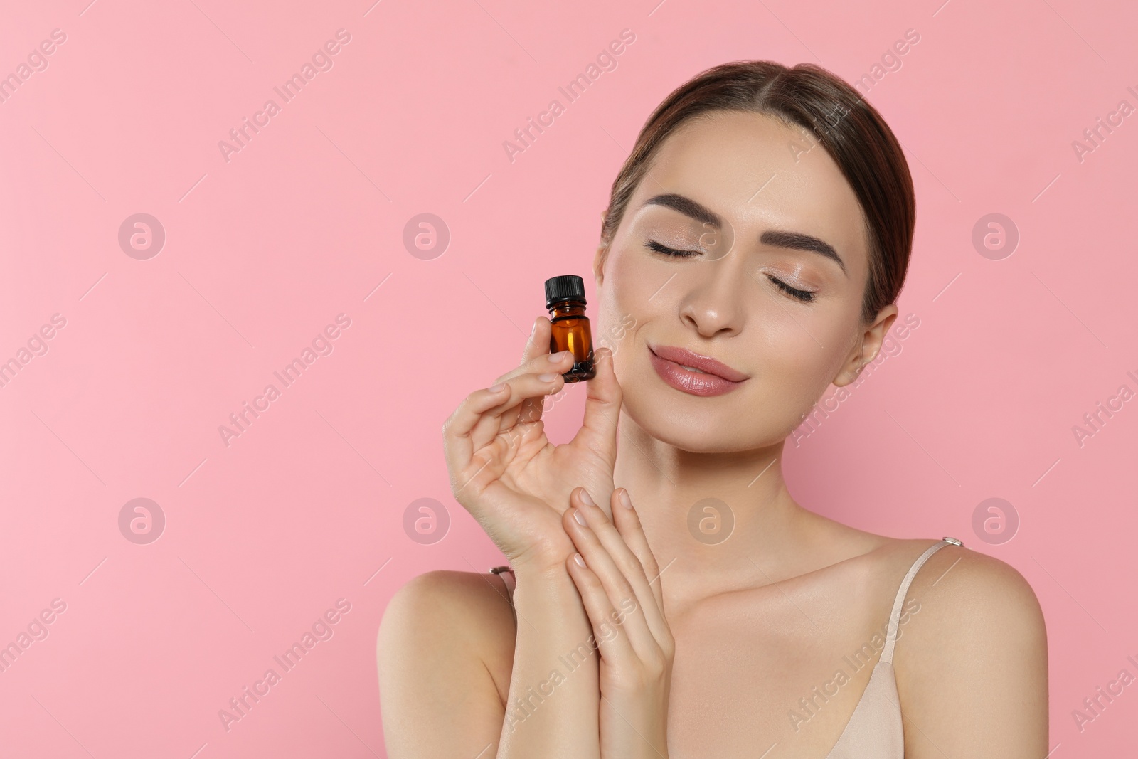 Photo of Young woman with bottle of essential oil on pink background, space for text