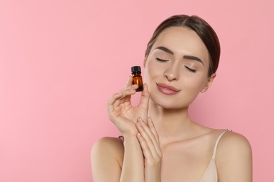 Young woman with bottle of essential oil on pink background, space for text