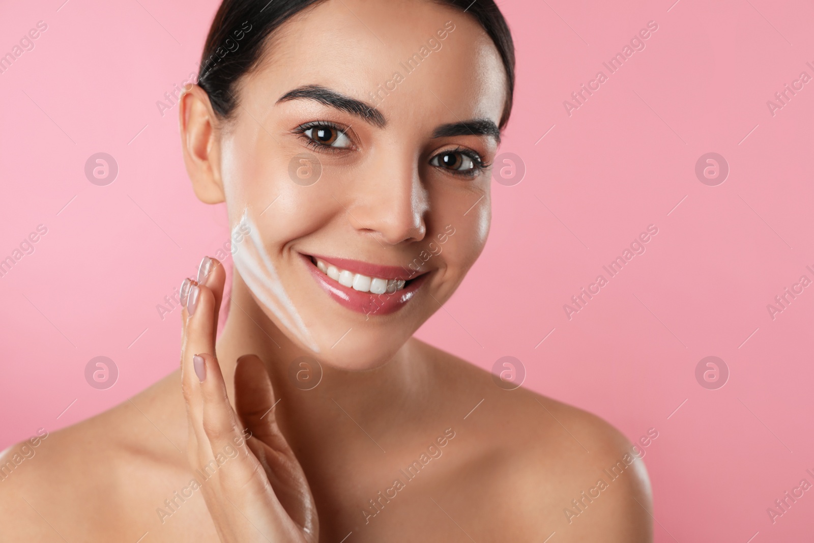 Photo of Young woman applying cosmetic product on pink background. Washing routine