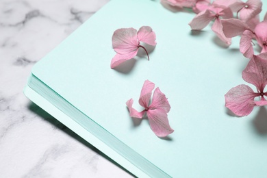 Photo of Open notebook and beautiful flowers on white marble table, closeup