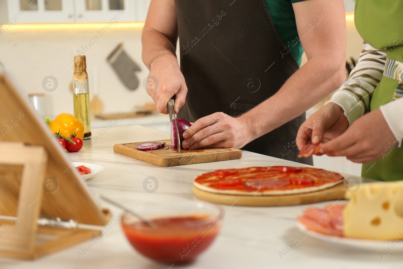 Photo of Couple making pizza together while watching online cooking course via tablet in kitchen, closeup