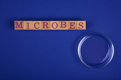 Photo of Word Microbes made with wooden cubes and magnifying glass on blue background, top view. Space for text