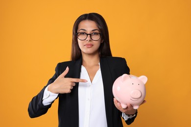 Photo of Young woman in eyeglasses with piggy bank on orange background