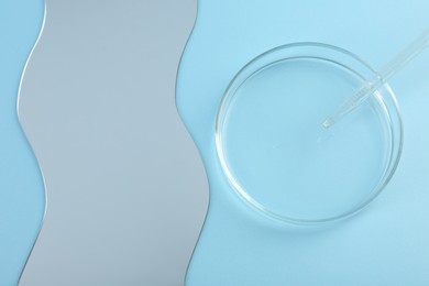 Empty petri dish, pipette and mirror on light blue background, flat lay