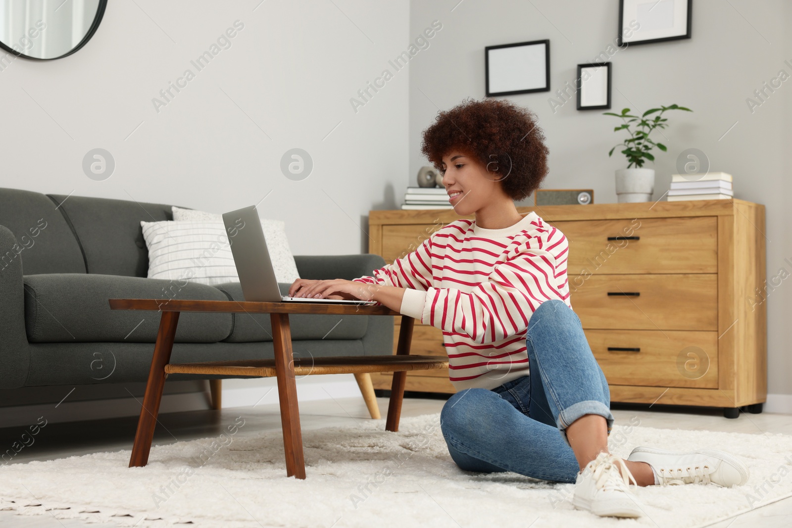 Photo of Beautiful young woman using laptop at wooden coffee table in room