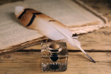 Feather pen, inkwell and old book on wooden table