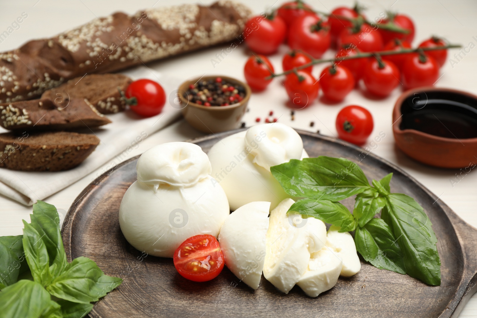 Photo of Delicious burrata cheese with basil and tomato on white table, closeup