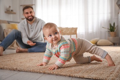 Photo of Happy young father watching his cute baby crawl on floor at home