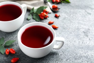 Photo of Fresh rose hip tea and berries on grey table, closeup. Space for text