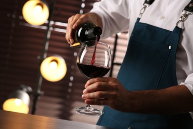 Photo of Bartender pouring red wine into glass indoors, closeup