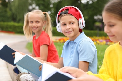 Cute boy in headphones and girls reading books in green park