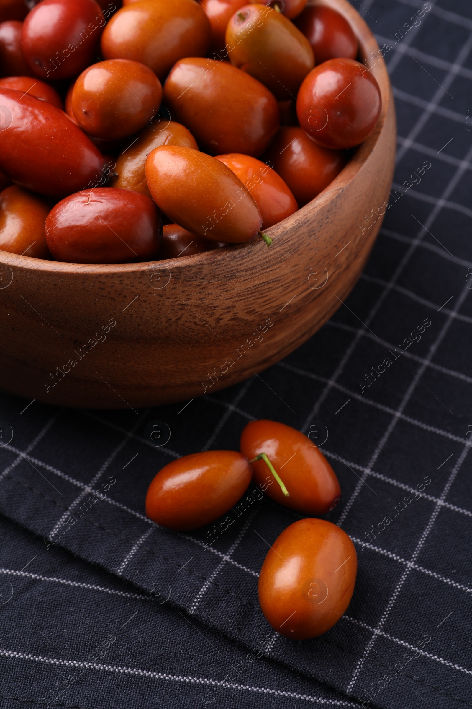 Photo of Wooden bowl with ripe red dates and napkin on table, closeup