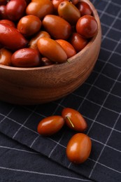 Wooden bowl with ripe red dates and napkin on table, closeup