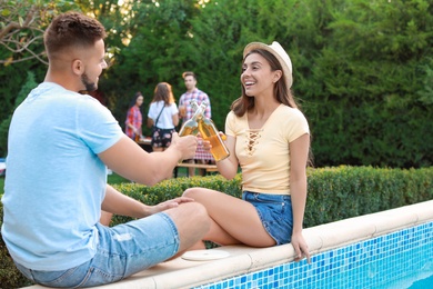 Photo of Happy friends with drinks at barbecue party near swimming pool outdoors