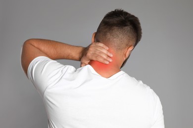 Man suffering from neck pain on grey background, back view