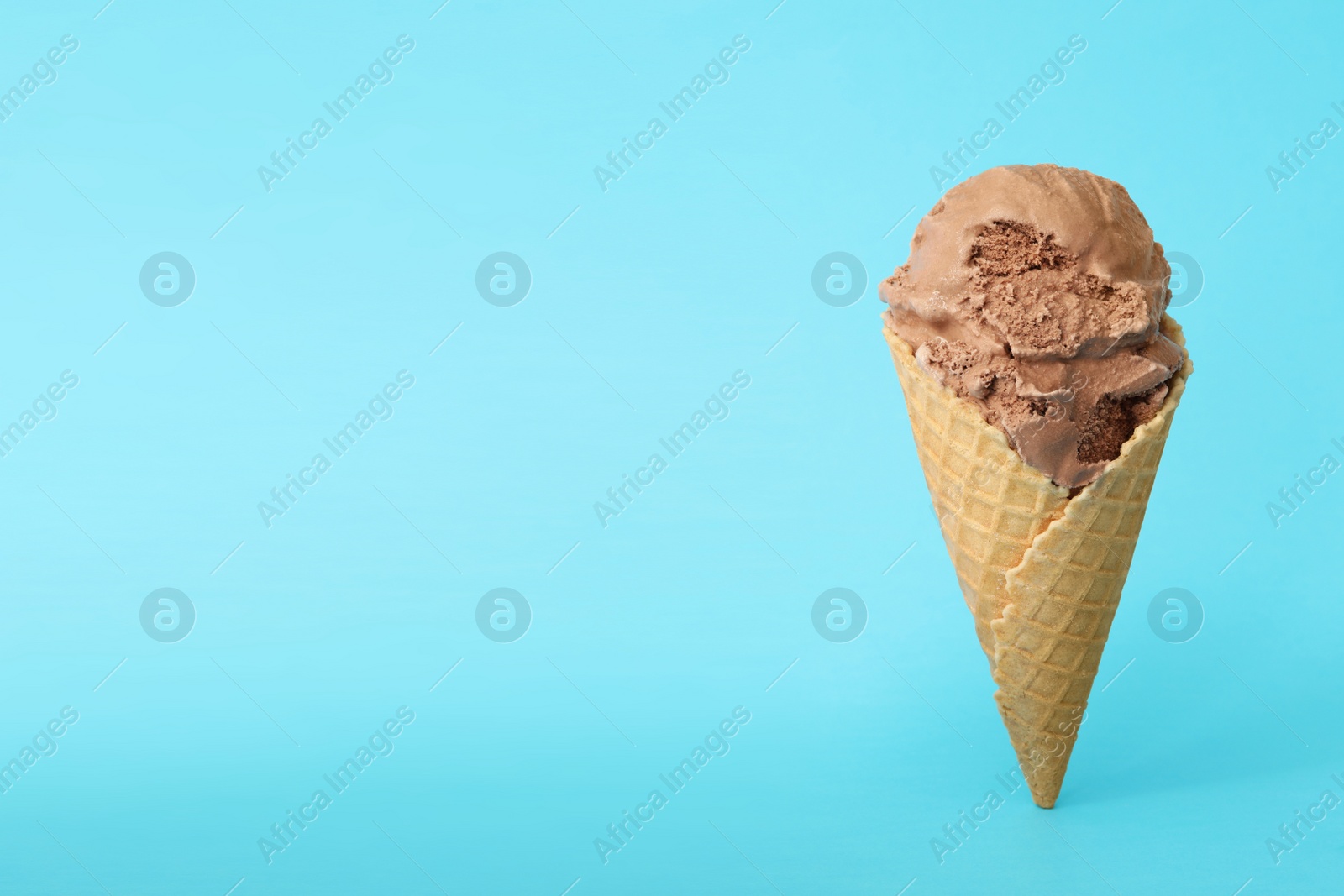 Photo of Delicious chocolate ice cream in waffle cone on light blue background. Space for text