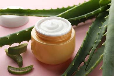 Jar with cream and cut aloe leaves on pink background, closeup