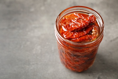 Photo of Jar of sun dried tomatoes on gray table with space for text