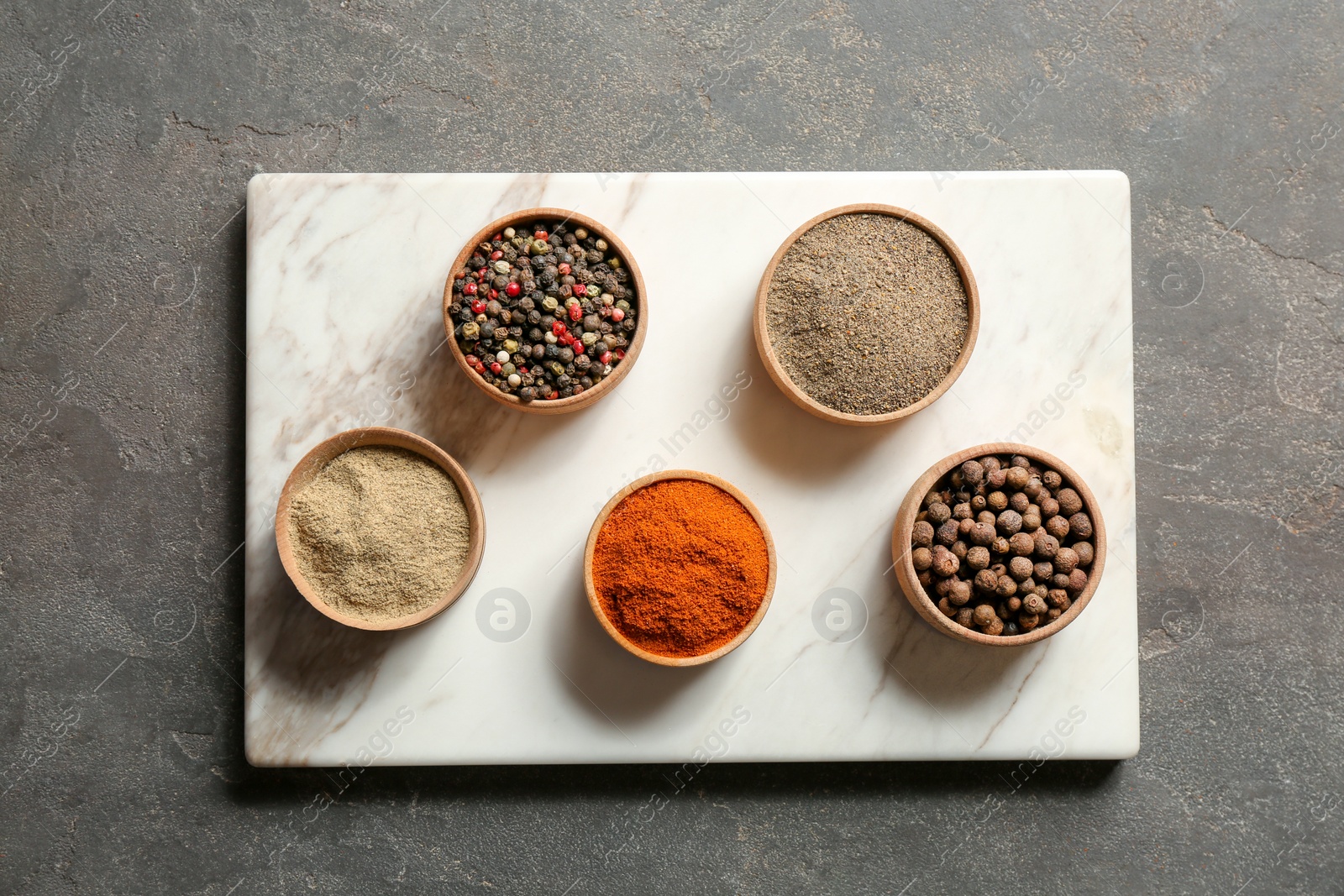 Photo of Marble board with different types of pepper in bowls on gray background, top view