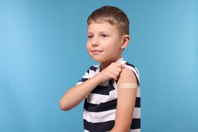 Photo of Boy with sticking plaster on arm after vaccination against light blue background