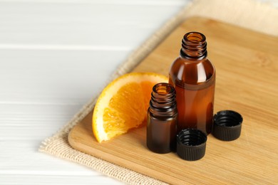 Photo of Bottles of essential oil and orange slice on white wooden table, closeup. Space for text