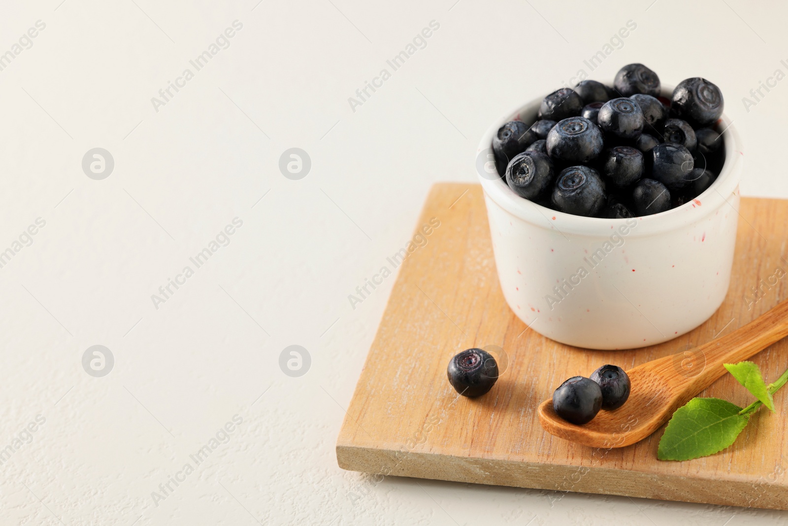 Photo of Ripe bilberries and leaves on white table. Space for text