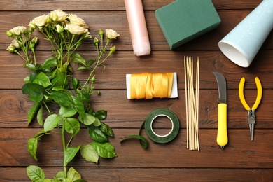 Florist equipment with flowers on wooden background, top view