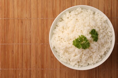 Bowl with delicious rice and parsley on bamboo mat, top view. Space for text