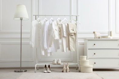 Photo of Rack with different stylish women`s clothes, shoes, lamp and dresser near white wall in room