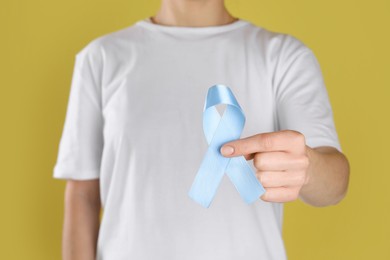 International Psoriasis Day. Woman with light blue ribbon as symbol of support on yellow background, closeup