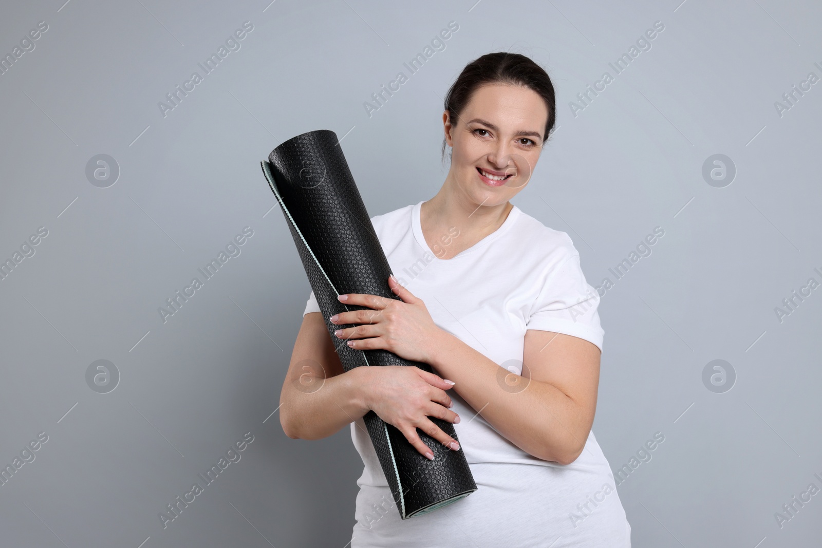 Photo of Happy overweight woman with yoga mat on grey background