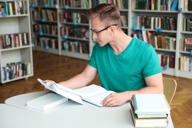 Photo of Young man reading book at table in library