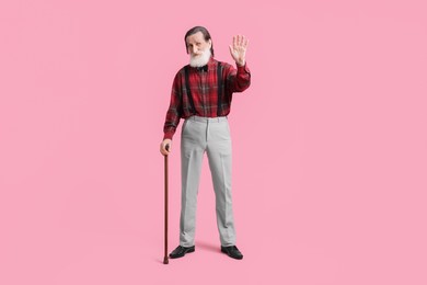 Photo of Senior man with walking cane waving on pink background