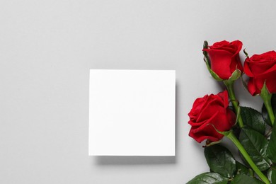 Photo of Blank card and beautiful red roses on gray background, flat lay. Space for text