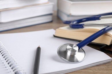 Photo of Student textbook, blank notebook, pencil and stethoscope on wooden table, closeup. Medical education