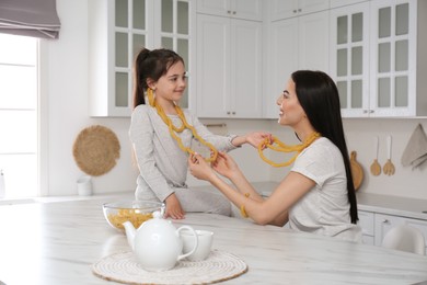 Photo of Young mother and her daughter with necklaces made of pasta having fun in kitchen