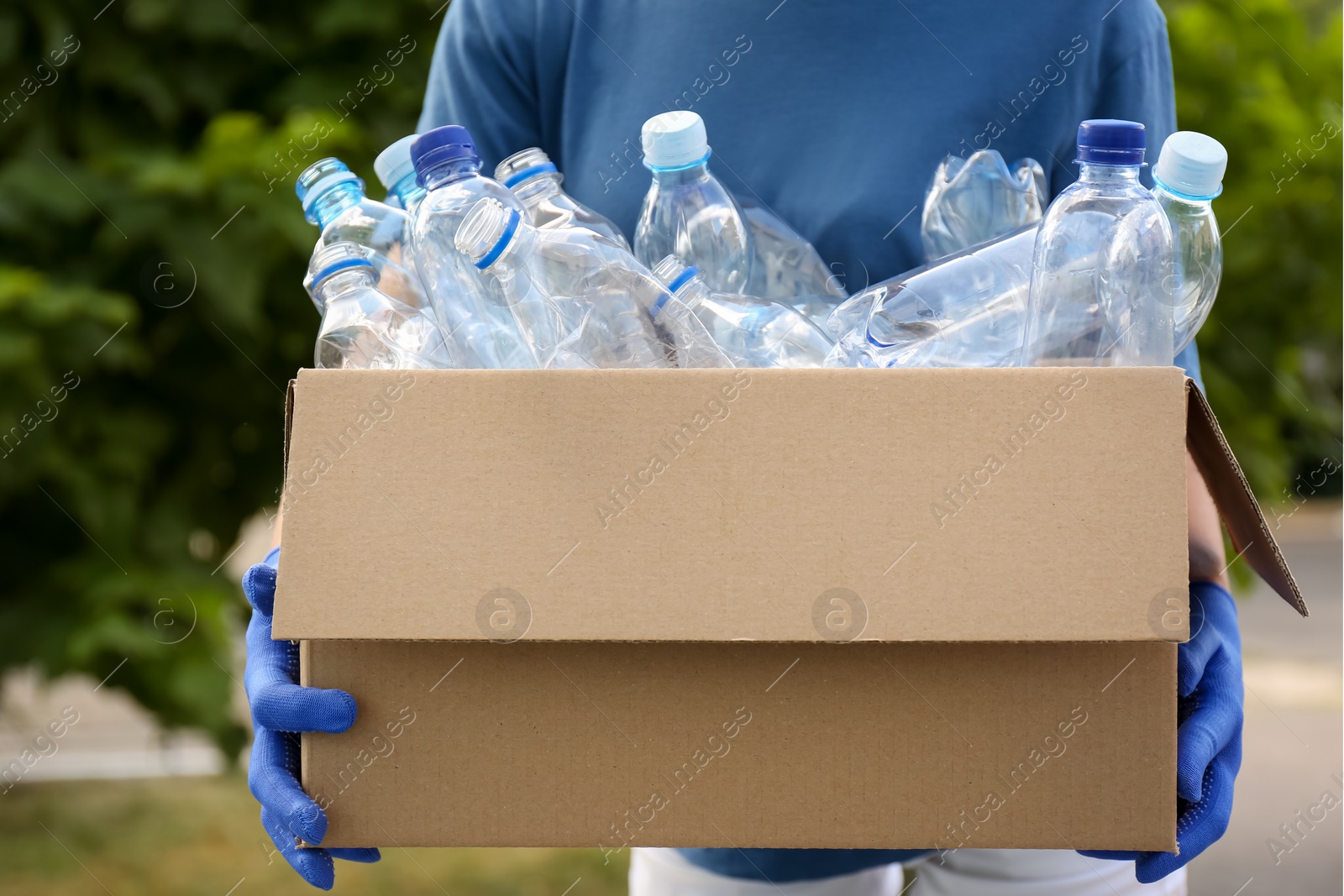 Photo of Woman holding cardboard box with used plastic bottles outdoors, closeup. Recycling problem
