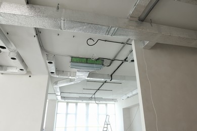 Ventilation system and wires on white ceiling indoors