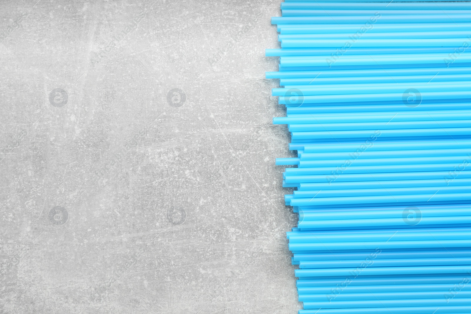 Photo of Light blue plastic drinking straws on grey stone table, flat lay. Space for text