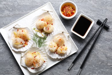 Photo of Raw scallops with spices, dill, lemon zest, shells and soy sauce on grey marble table, flat lay