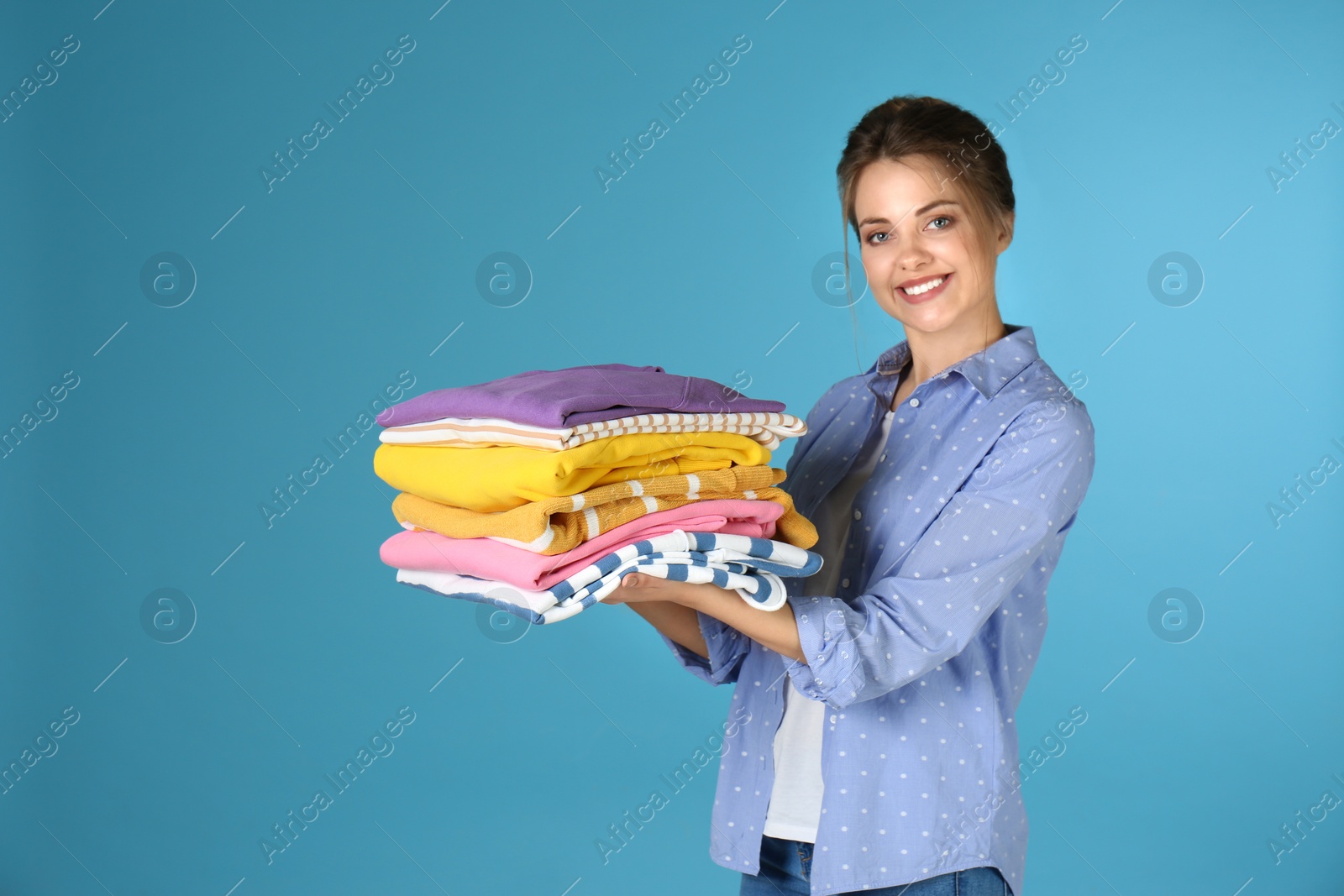 Photo of Happy young woman holding clean laundry on color background