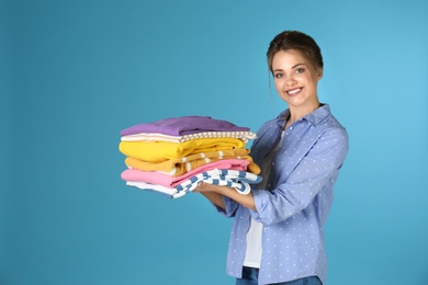 Happy young woman holding clean laundry on color background