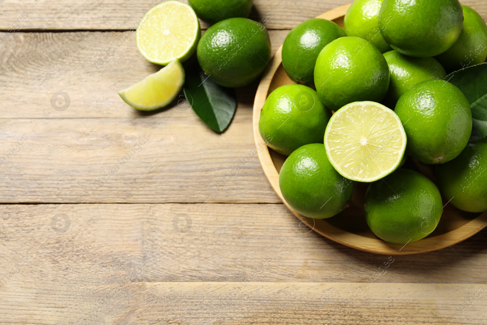 Photo of Fresh limes and green leaves on wooden table, flat lay. Space for text