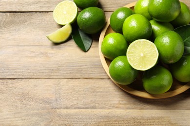 Fresh limes and green leaves on wooden table, flat lay. Space for text