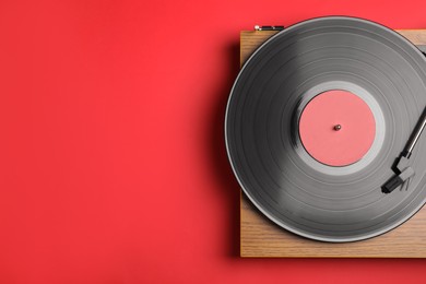 Photo of Modern vinyl record player with disc on red background, top view. Space for text