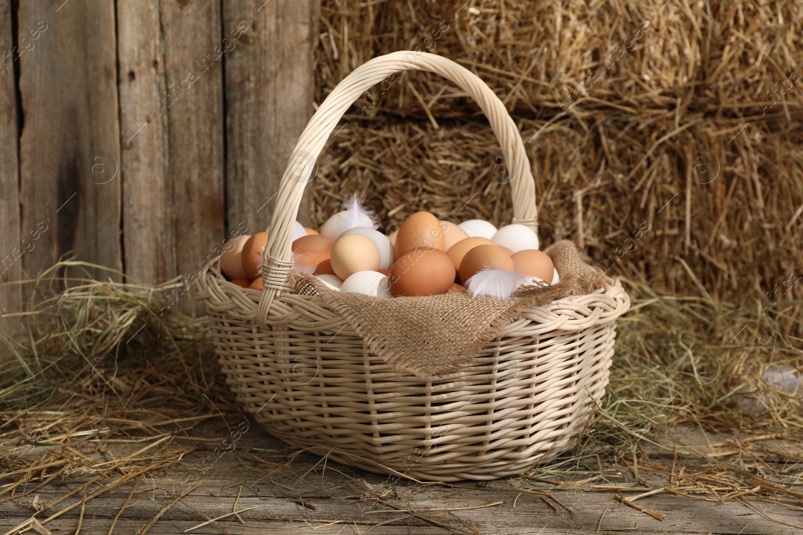 Photo of Wicker basket with fresh chicken eggs and dried straw in henhouse