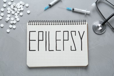Photo of Notebook with word Epilepsy, stethoscope, pills and syringes on grey table, flat lay