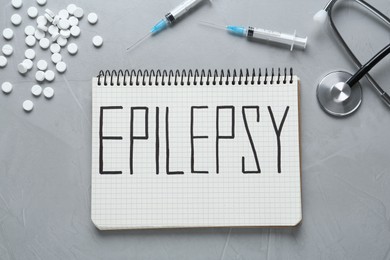 Notebook with word Epilepsy, stethoscope, pills and syringes on grey table, flat lay