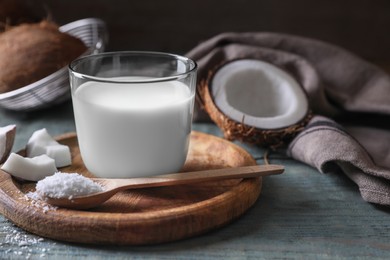 Glass of delicious coconut milk, spoon with flakes and nuts on wooden table, space for text