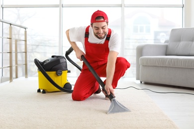 Male worker cleaning carpet with vacuum in living room